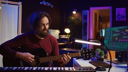 Portrait of artist recording tunes on daw software with his guitar, enjoying time in his home studio office. Audio engineer and musician creating new tracks, stereo electronic instruments. Camera B.
