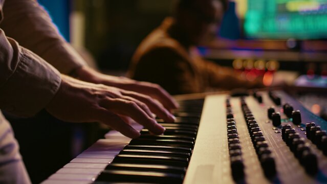 Musician composer playing midi controller synthesizer in professional studio, composing music on mixing console. Artist performing on piano electronic keyboard in control room. Camera B.