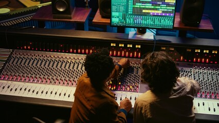 Musician and audio technician collaborating on mixing tracks to create a successful hit in...