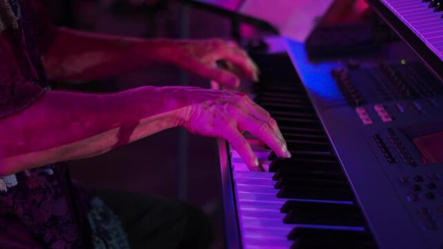 Close up a las manos de un hombre tocando el piano en un escenario de noche con luz morada.