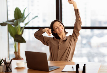 Time For Break. Successful young female manager stretching hands at workplace and smiling, free...