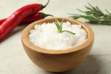 Sea salt in bowl, rosemary and chili peppers on grey table, closeup