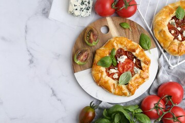 Tasty galettes with tomato, basil and cheese on white marble table, flat lay. Space for text