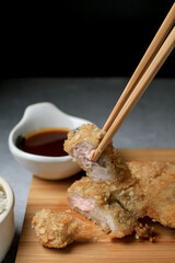 Hand use chopstick eating Japanese tonkatsu fried pork cutlet recipe with sweet sour sauce and rice on wooden broad. Asian food.
