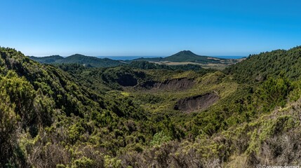 Fototapeta premium A panoramic view of a volcanic crater in a lush green valley, with a distant mountain range and ocean in the background.
