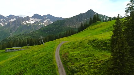 Aerial view cyclist riding road bike through ski resort in Alps in summer. Bicyclist travels on gravel bicycle through mountain resort in Bavarian mountains, Germany. Cycling trips at alpine slopes 