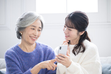 リビングで笑顔で話す、スマホを見ながら過ごす仲良し親子(母と娘)