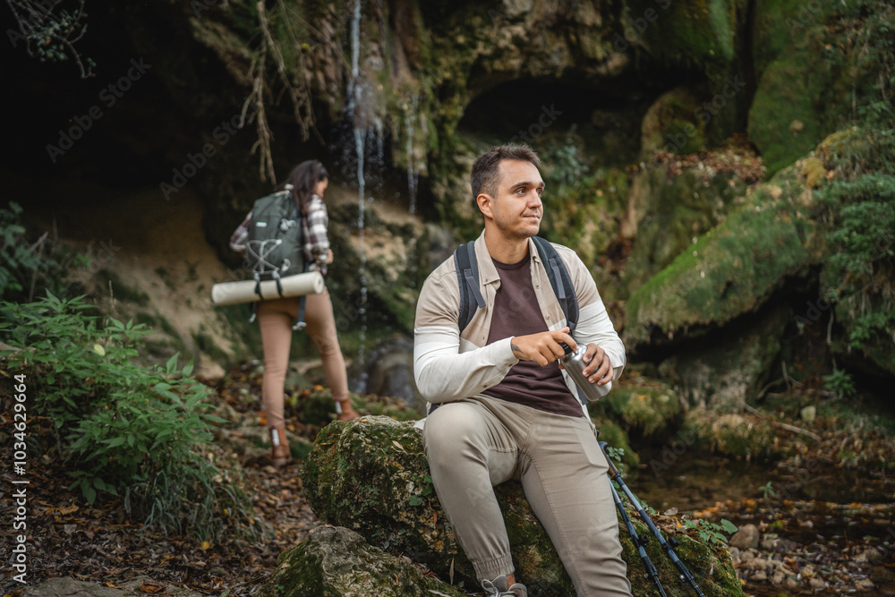 Wall mural Adult man hiker backpacker have a rest and drink from metal bottle