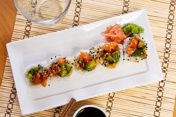 Rectangular narrow white plate with traditional Asian food sits on bamboo napkin. Saketaki rolls...