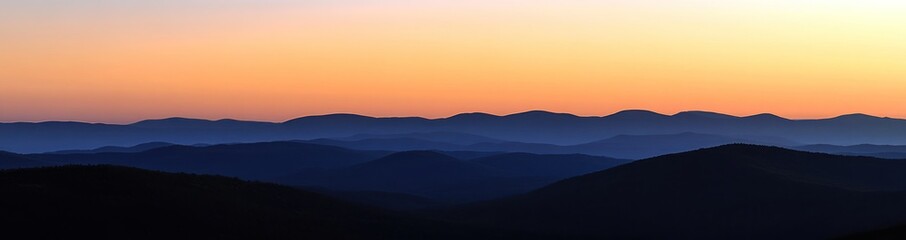 Silhouetted mountain range at sunrise with soft, hazy light and a blurred background.