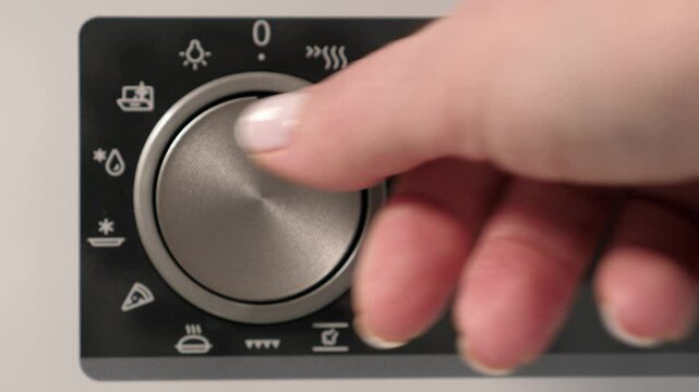 Woman adjusting modern white oven in kitchen. Female hand pushing and turning knobs on oven control panel. Closeup
