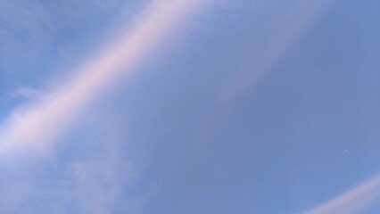 A beautiful sky with a faint rainbow arc. The sky is predominantly blue with some white clouds. The rainbow is subtle, with pastel shades of pink, purple, and orange.