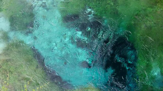 Water flows out of a karst cave in a powerful stream. The stream of water beats from under the ground. A beautiful landmark of Albania - Blue Eye. An underground river flows out.
