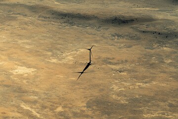 solitary wind turbine in the middle of a vast desert, its blades casting long shadows on the ground