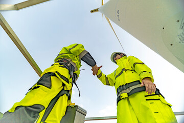 A team of engineers celebrates success after completing wind turbine maintenance at a wind farm....