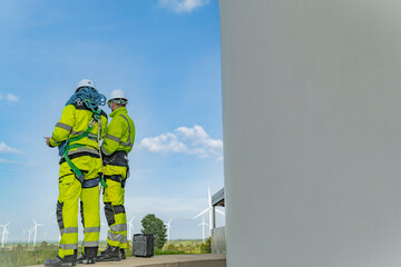 A team of engineers inspects and maintains a large wind turbine at a renewable energy wind farm....