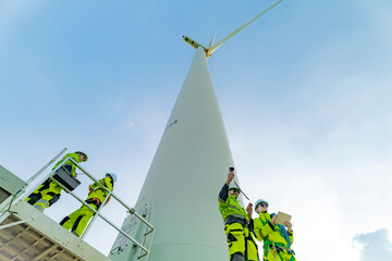 A team of engineers inspects and maintains a large wind turbine at a renewable energy wind farm....