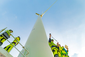 A team of engineers inspects and maintains a large wind turbine at a renewable energy wind farm....