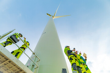 A team of engineers inspects and maintains a large wind turbine at a renewable energy wind farm....