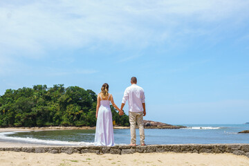 couple on the beach with their backs turned, dressed in white