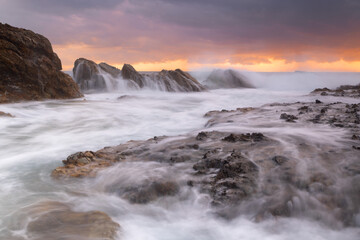 Dramatic coastline. Waves crash over large sea side rocks creating cascading waterfalls