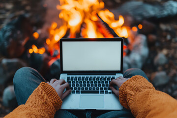 Person using laptop by campfire setting