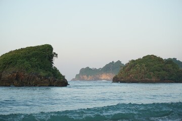 Beautiful natural scenery front of the island on the sea under bright blue sky in summer at Kondang Merak Banyu Meneng Malang Tropical Beach, East Java.