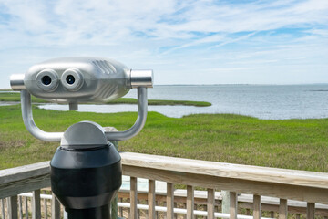 metal binoculars mounted on heavy pedestal near a wooden fence on a nature area observation deck for birding, whale watching and wildlife viewing