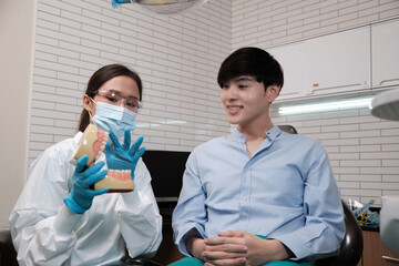 Asian female dentist explaining orthodontic care and whitening to young male patient with teeth...