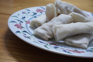 Heap of raw spring rolls(lumpia) on the plate. Frozen food on wooden tables.