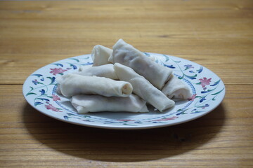 Heap of raw spring rolls(lumpia) on the plate. Frozen food on wooden tables.