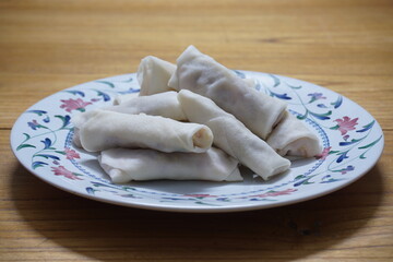 Heap of raw spring rolls(lumpia) on the plate. Frozen food on wooden tables.