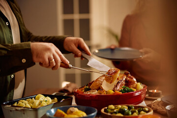 Close up of man carving Thanksgiving turkey during meal at dining table.