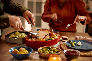 Cloe up of man carving roast turkey during Thanksgiving dinner in dining room.