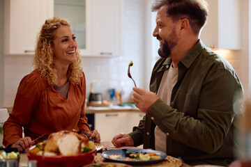 Cheerful couple communicating while eating at dining table on Thanksgiving.