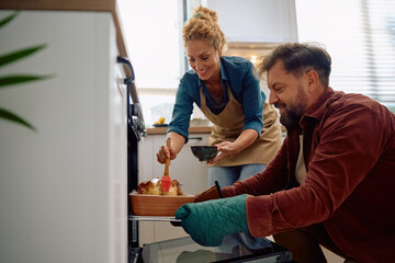 Happy couple cooperating while roasting turkey in oven for Thanksgiving.