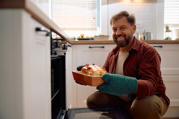 Happy man with freshly roasted turkey in kitchen looking at camera.