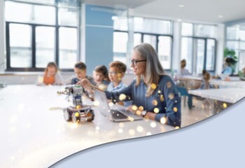 A blurred image of a classroom setting with a teacher and students working on a robotic project. The room is brightly lit with bokeh lights in the foreground.