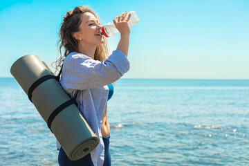 Smiling young fitness yoga woman drink pure water blue sea sky beach coastline closeup