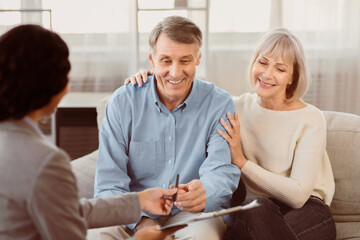 Happy senior couple about to sign document at meeting with financial advisor, female consultant...