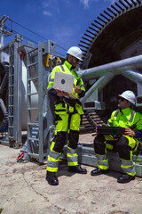 Maintenance engineer team standing at windmills at wind turbine farm. Group of people wear safety helmet and uniform working at alternative renewable energy wind station. Sustainable energy technology