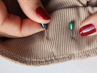 The hands of a seamstress fasten the edges of the fabric with a Platonic pin. Using dressmaker's...