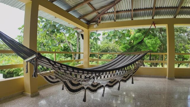 Nylon handmade hammock swinging in the wind, on a covered porch with a lush, tropical garden view