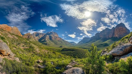 Obraz premium A panoramic view of a mountain valley with lush green vegetation, rocky outcrops, and a bright blue sky with white clouds.