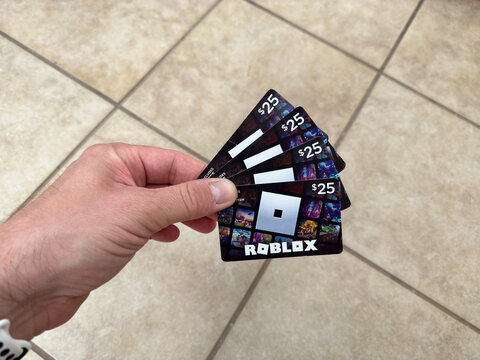 Hand holding 4 Robux gift cards for Roblox online games.