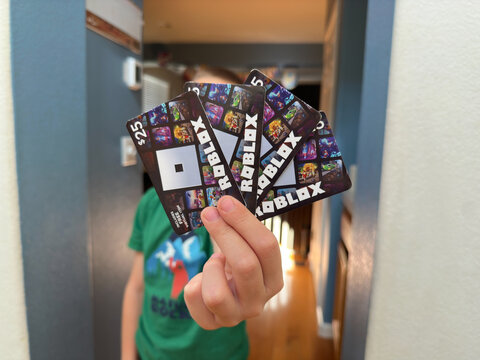 Holding 4 pack of Roblox video game gift cards to purchase Robux.