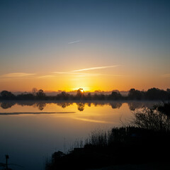 Obraz premium Sunrise over a calm lake, symbolizing tranquility, renewal, and the beauty of nature