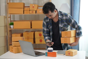 Entrepreneur of young Asian man working with laptop computer and boxes for ordering packaging from online shopping at home for SME business online