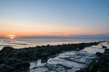 A stunningly beautiful sunset is painting vibrant colors across a tranquil sea and its rocky...