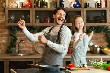 Cooking With Fun. Portrait Of Cheerful Little Girl And Her Dad Dancing In Kitchen, Enjoying Spending Time Together